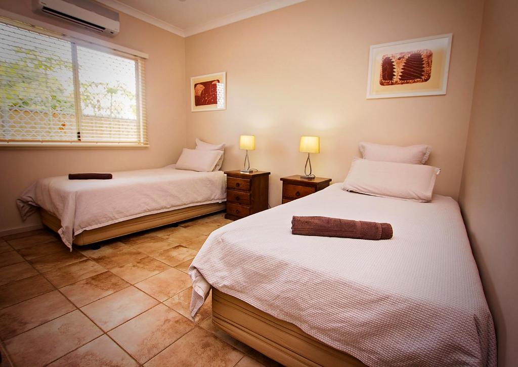 two beds in a room with two lamps and a window at Wunan House in Kununurra
