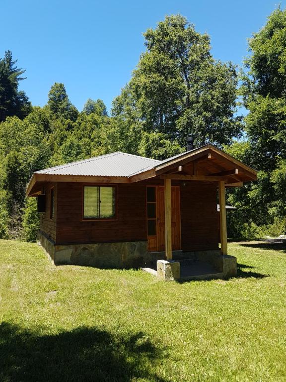 una pequeña cabaña en un campo de césped con árboles en Cabañas Los Maquis, en Pucón