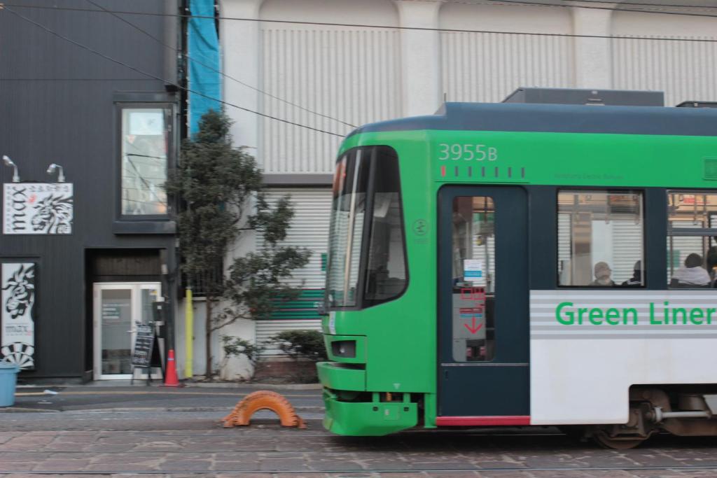 a green and white bus parked on a street at Guesthouse COCO Hiroshima (Female Only) in Hiroshima