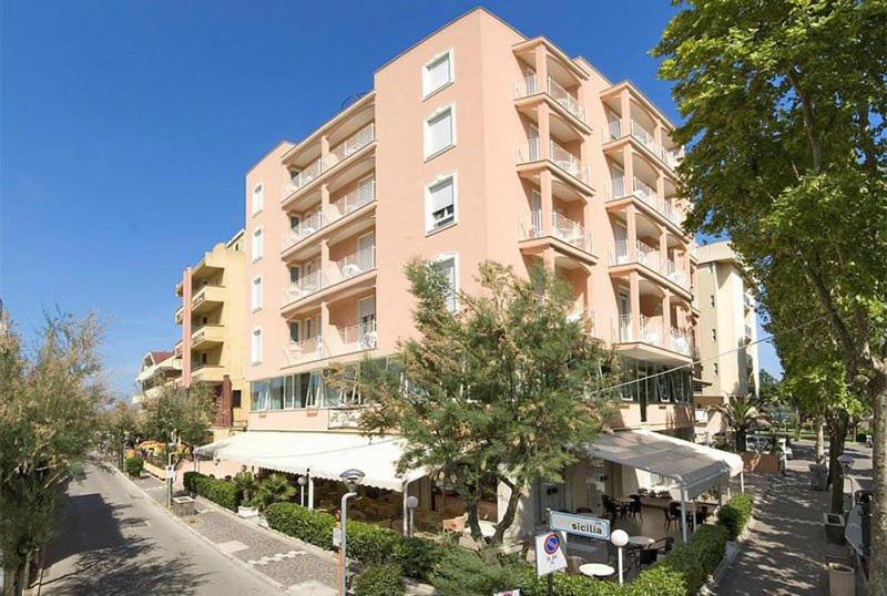 un grand bâtiment rose avec un restaurant en face de lui dans l'établissement Hotel Nettuno, à Misano Adriatico