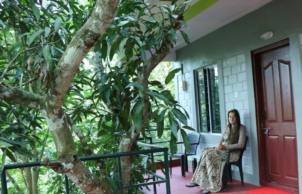 a woman sitting on a porch next to a tree at Periyar Green Bed & Breakfast in Thekkady