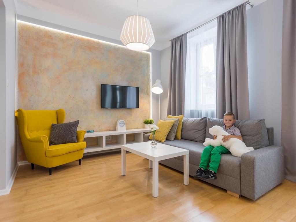 Around Market Square Apartments في كراكوف: طفل صغير يجلس على أريكة يحمل دمية دب