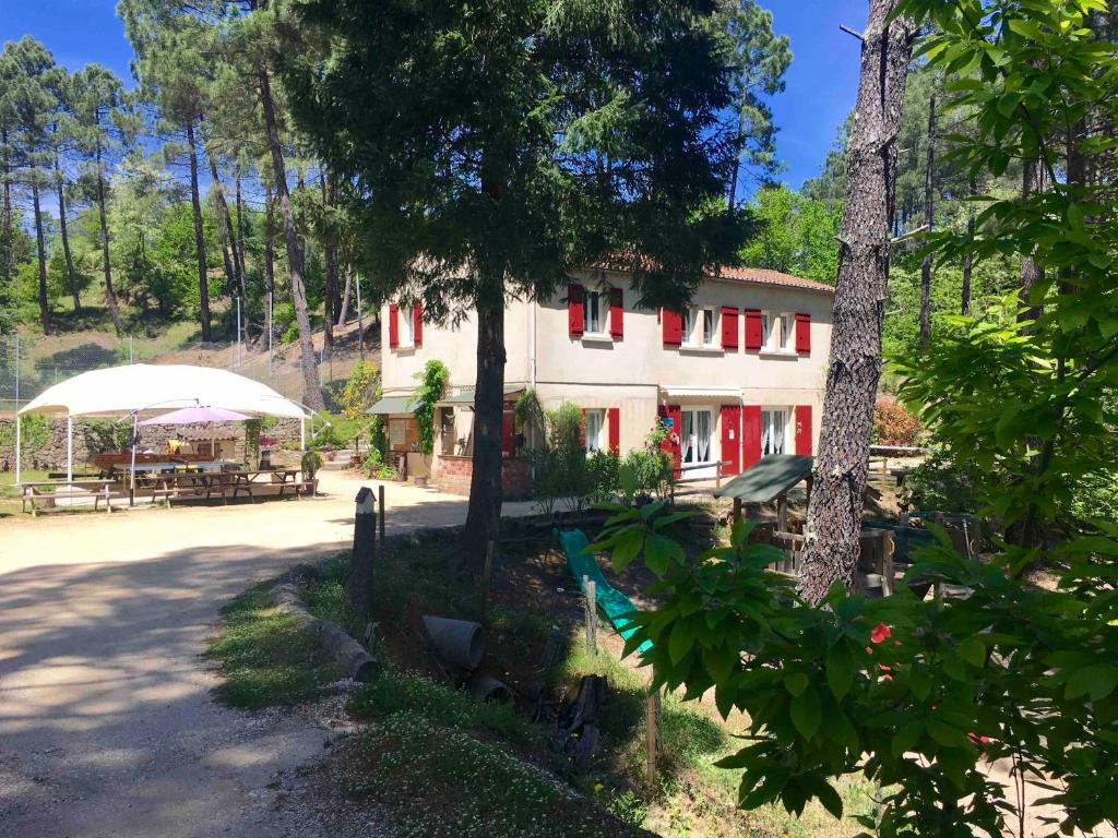 ein Gebäude mit roten Fenstern, einem Tisch und einem Sonnenschirm in der Unterkunft Village de gîtes Ravel in Saint-Jean-du-Gard