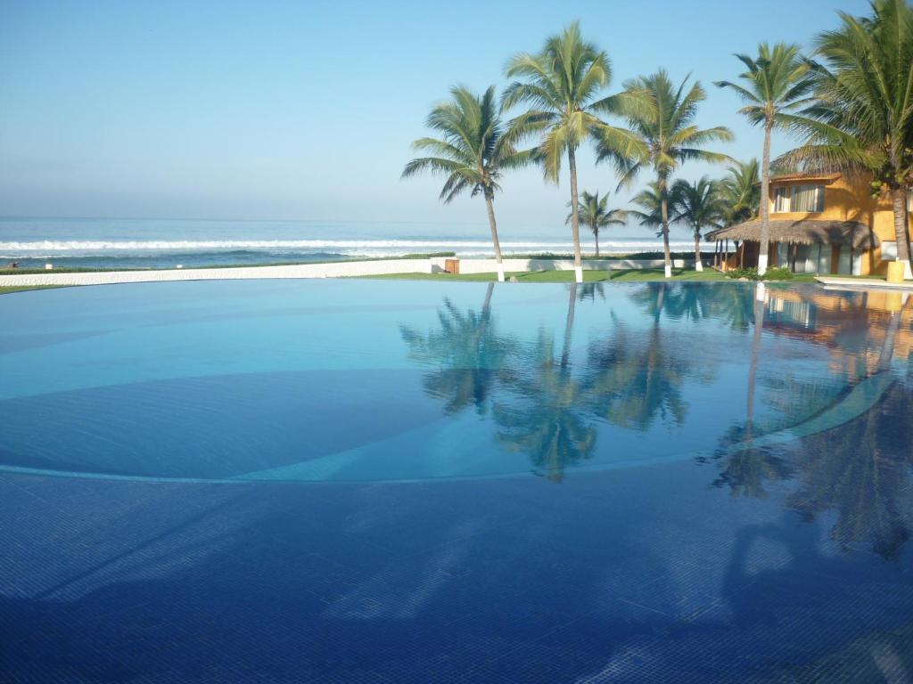 a swimming pool next to a beach with palm trees at Villas Playa Blanca in Zihuatanejo