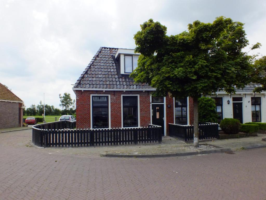 a red brick house with a black fence and a tree at Gezellig en knus huisje vlakbij het wad in Holwerd