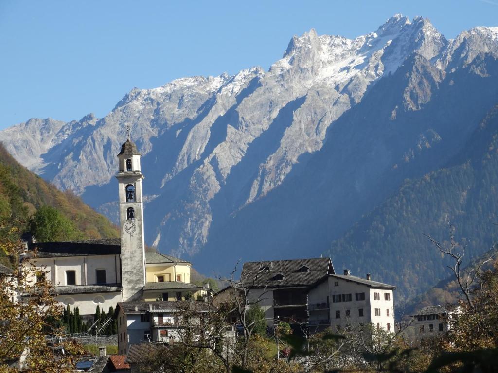 a building with a clock tower in front of a mountain at Casetta Villa in Villa di Chiavenna