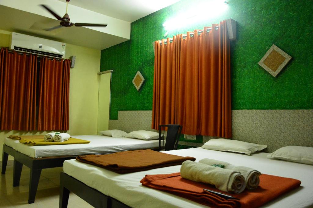 a room with three beds with green walls and orange curtains at Hotel Madhava in Shirdi