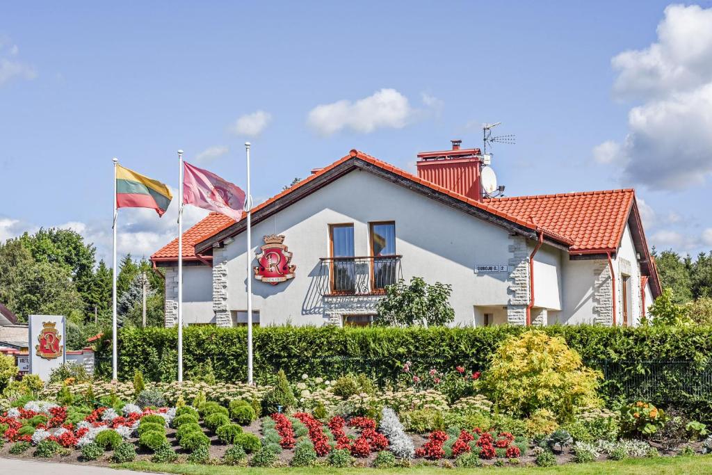 a white house with flags in front of a garden at Villa Regina - Apartment Complex Resort in Šventoji in Šventoji