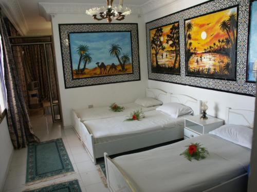 Habitación con 2 camas y pinturas en la pared. en Hotel Hamilton en Hammamet