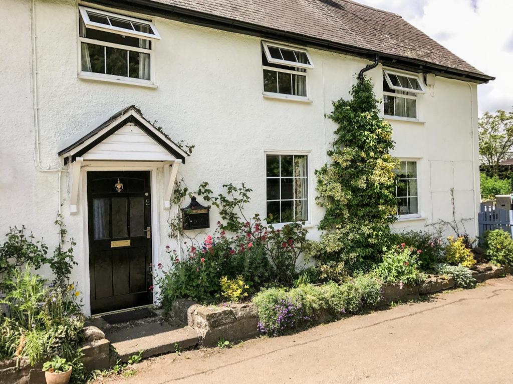 a white house with a black door and some flowers at George Cottage in Clun