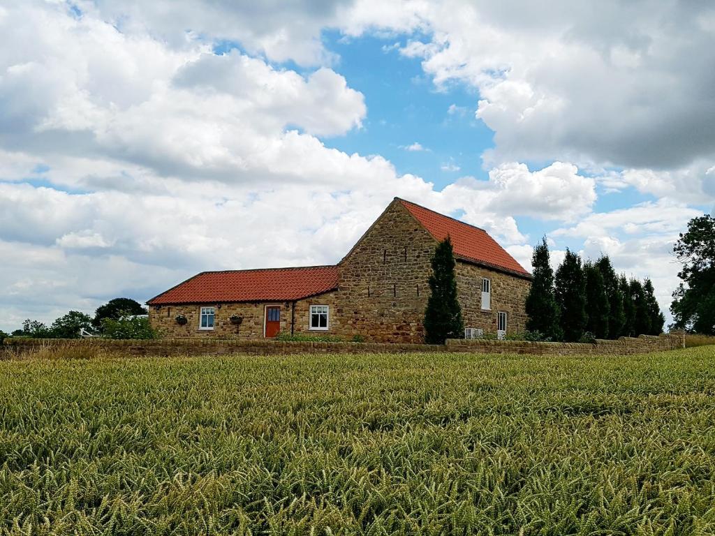 um celeiro de tijolos com um telhado vermelho num campo em Bell House Barn em Staindrop