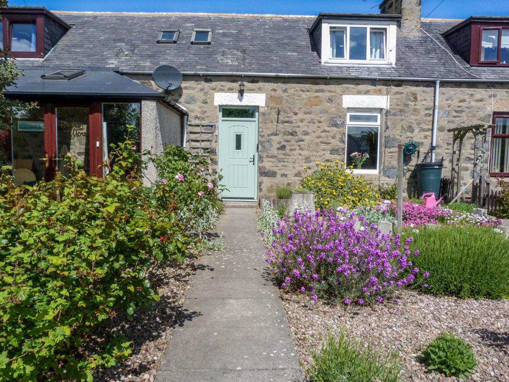 a stone house with a green door and flowers at 5 Distillery Cottages in Whitehills