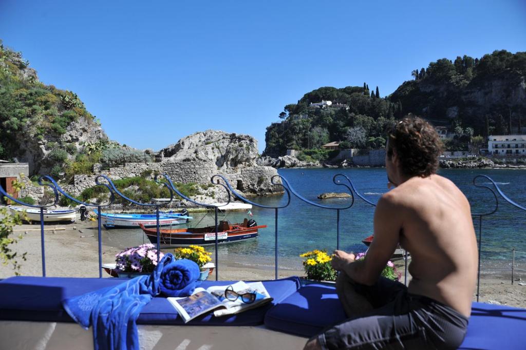 a man sitting on a table next to the water at La Prua in Taormina