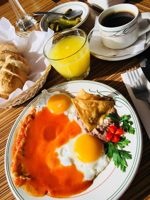 A breakfast setting with eggs in red sauce, toast, orange juice, coffee, and pickled vegetables.