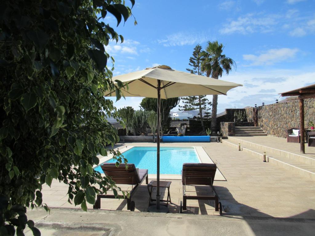 ein Pool mit einem Sonnenschirm, 2 Stühlen und einem Tisch mit einem Sonnenschirm in der Unterkunft El Cercado in Tías