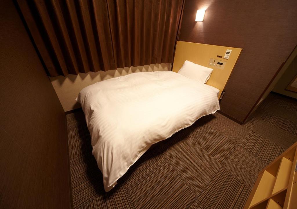 - duże białe łóżko w niewielkim pokoju w obiekcie Dormy Inn Hiroshima w mieście Hiroszima