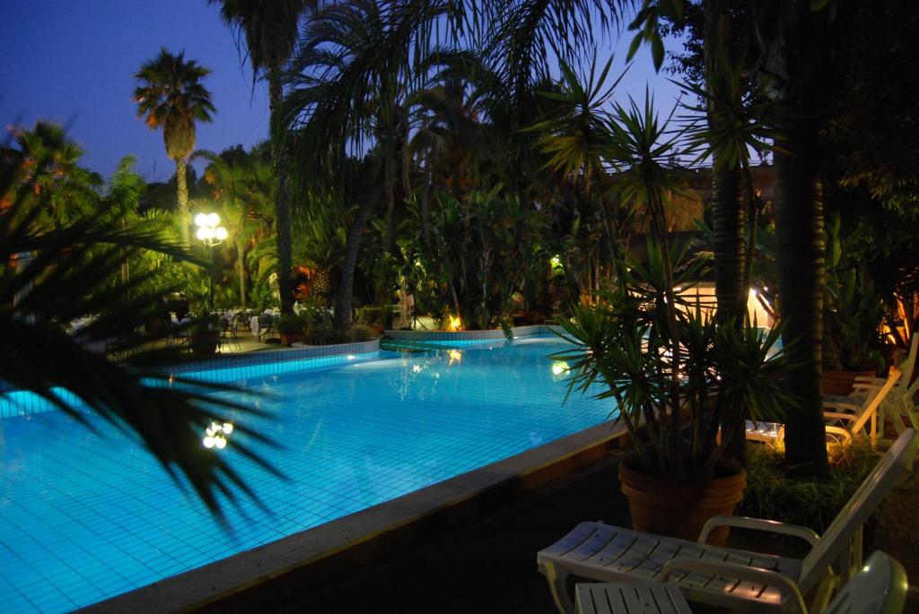 a swimming pool with palm trees at night at Garden Rooms in San Giovanni la Punta