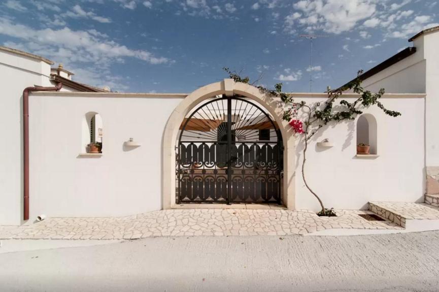 a white building with a black gate with flowers at Agriturismo Fontanelle in Otranto