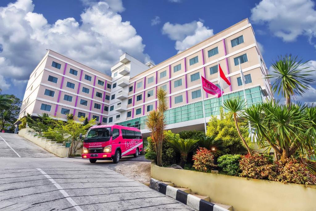 una furgoneta rosa estacionada frente a un edificio rosa en d'primahotel Balikpapan, en Balikpapan