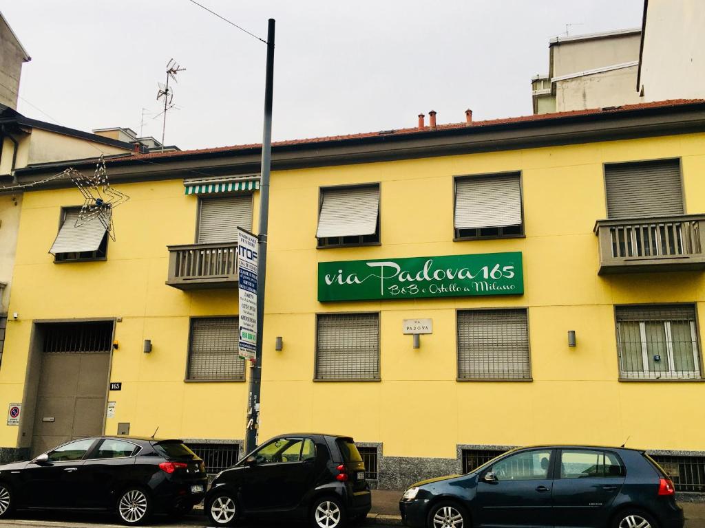 dos coches estacionados frente a un edificio amarillo en Via Padova 165 en Milán