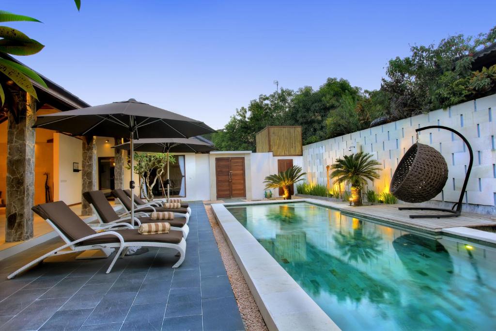 a swimming pool with lounge chairs and an umbrella at Villa Esperanto Seminyak in Seminyak