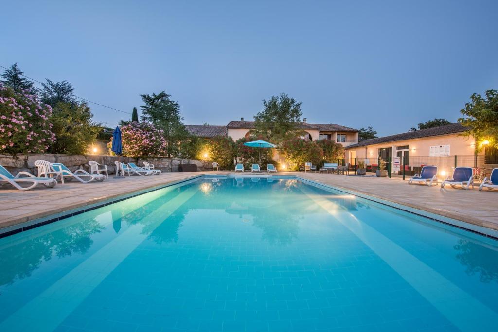 a swimming pool at night with chairs and umbrellas at Le Clos des Bruyères in Vallon-Pont-dʼArc