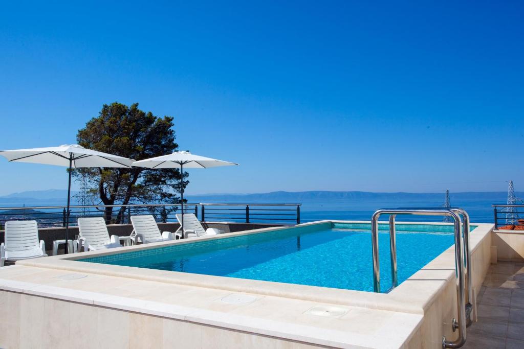 a swimming pool with chairs and umbrellas next to the ocean at Whitehouse Apartments in Makarska