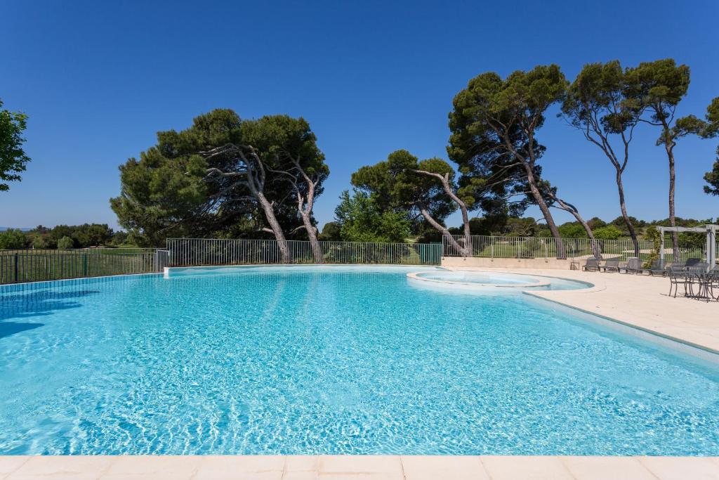 ソルマーヌ・ド・ボークリューズにあるMadame Vacances Domaine du Provence Country Club Service Premiumの青い水と木々が茂るスイミングプール