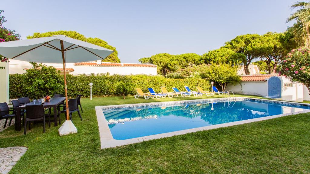 uma piscina com uma mesa e cadeiras e um guarda-sol em Villa Girassol em Vilamoura