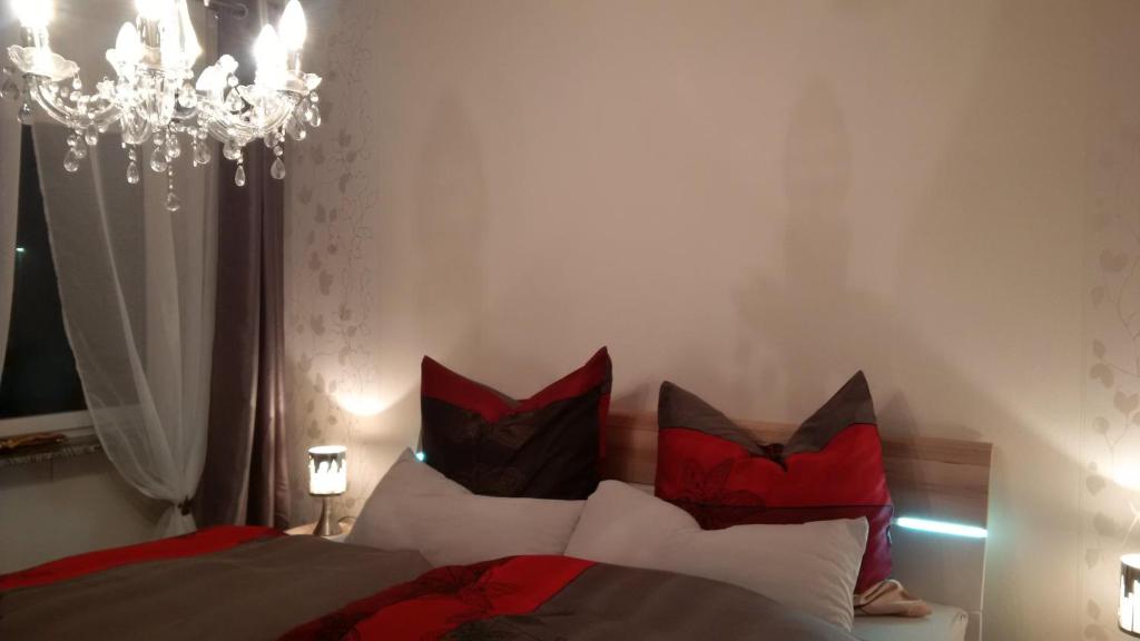 Schlafzimmer mit einem Bett mit roten Kissen und einem Kronleuchter in der Unterkunft Ferienhaus Rosemarie in Breungeshain