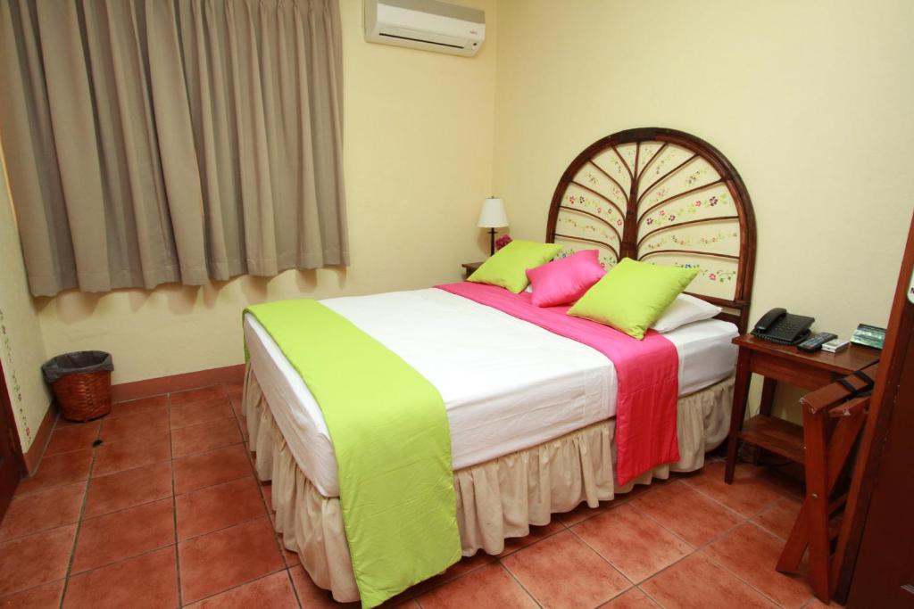 a bedroom with a bed with green and pink pillows at Hotel Colibri in Managua