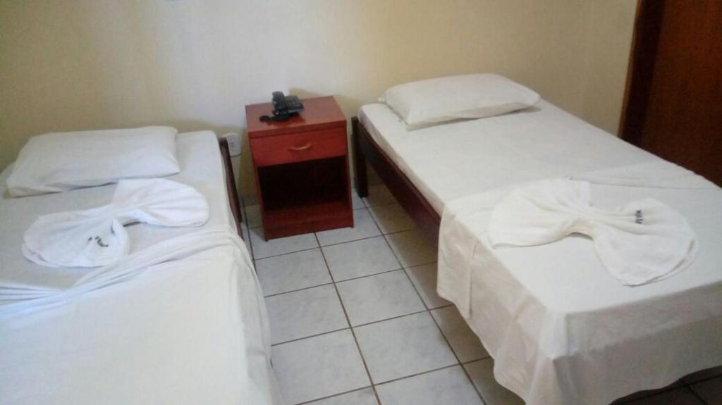 a room with two beds with white sheets and a table at Hotel Fênix in Barreiras