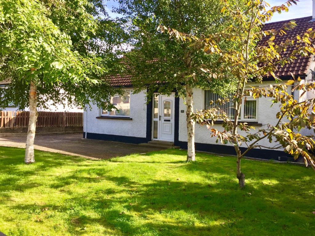 ein weißes Haus mit Bäumen im Hof in der Unterkunft Coolfinn Cottage in Ballycastle