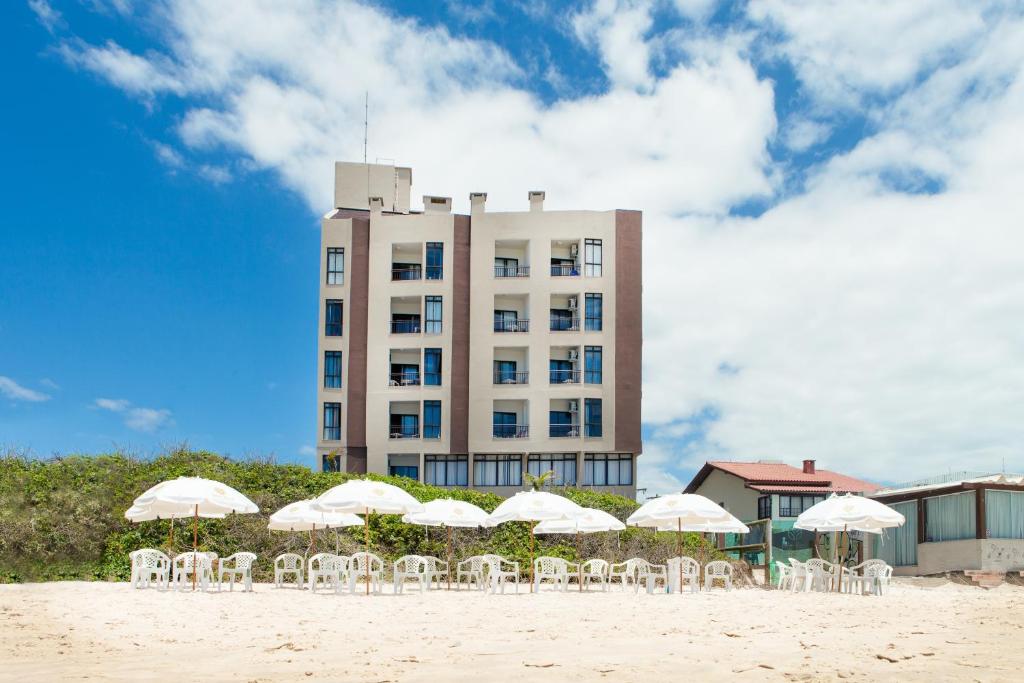 um edifício com cadeiras brancas e guarda-sóis na praia em Palm Beach Apart Hotel em Florianópolis