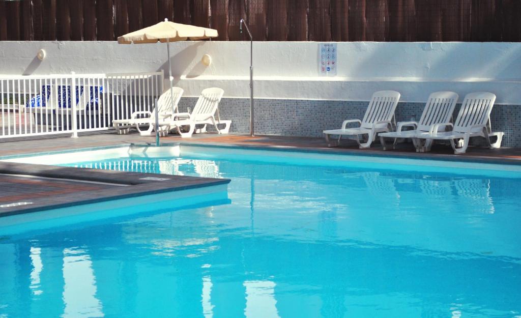 a swimming pool with white chairs and an umbrella at Apartamentos Calma in Playa del Ingles