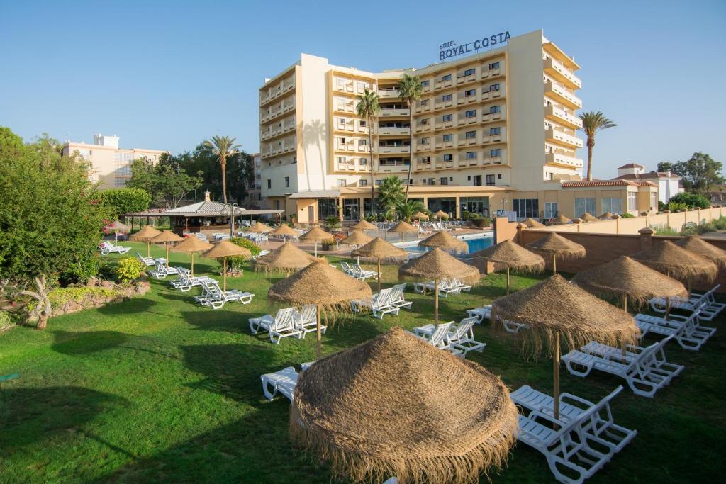 un grupo de sillas y sombrillas de paja frente a un hotel en Royal Costa, en Torremolinos