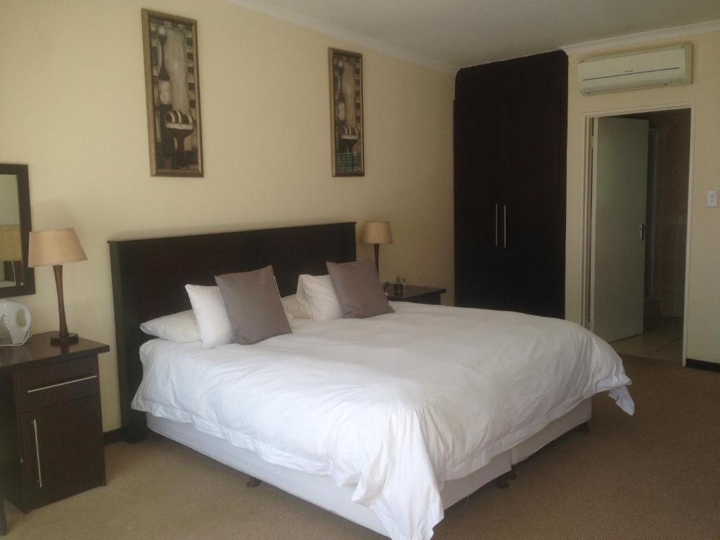 1 dormitorio con 1 cama grande con sábanas y almohadas blancas en The Lazy Grape Guest Lodge & Spa, en Benoni