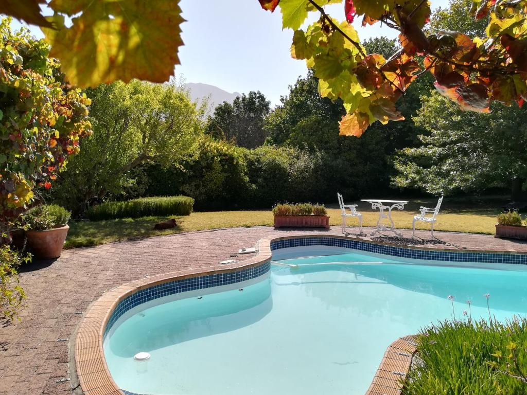 een zwembad in een tuin met een tafel en stoelen bij Le Petit Vignoble in Kaapstad