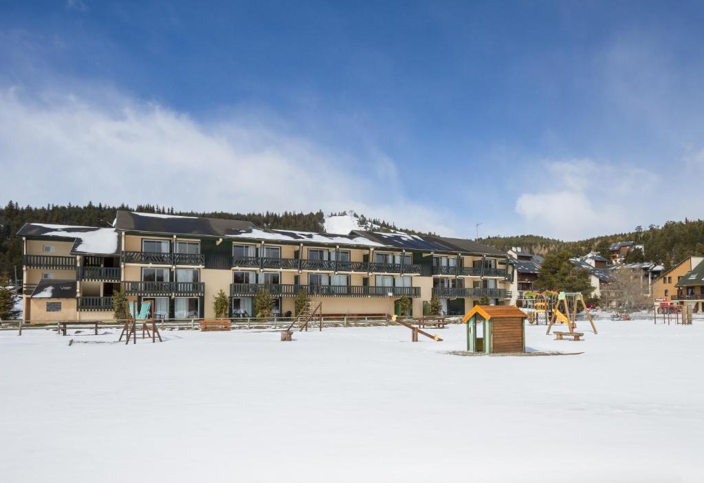 a large building in the snow with a playground at Residence Le Sequoia - maeva Home in Bolquere Pyrenees 2000