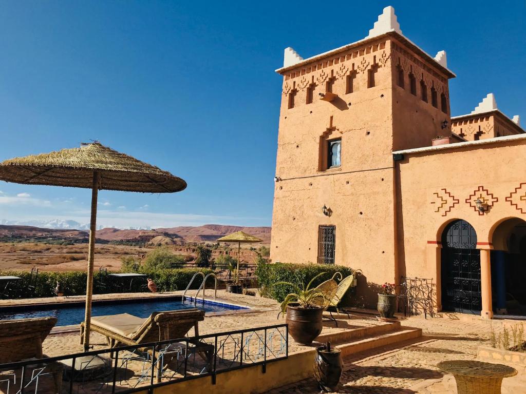 a building with a pool and an umbrella at Kasbah Rayane Ait Ben Haddou in Aït Ben Haddou