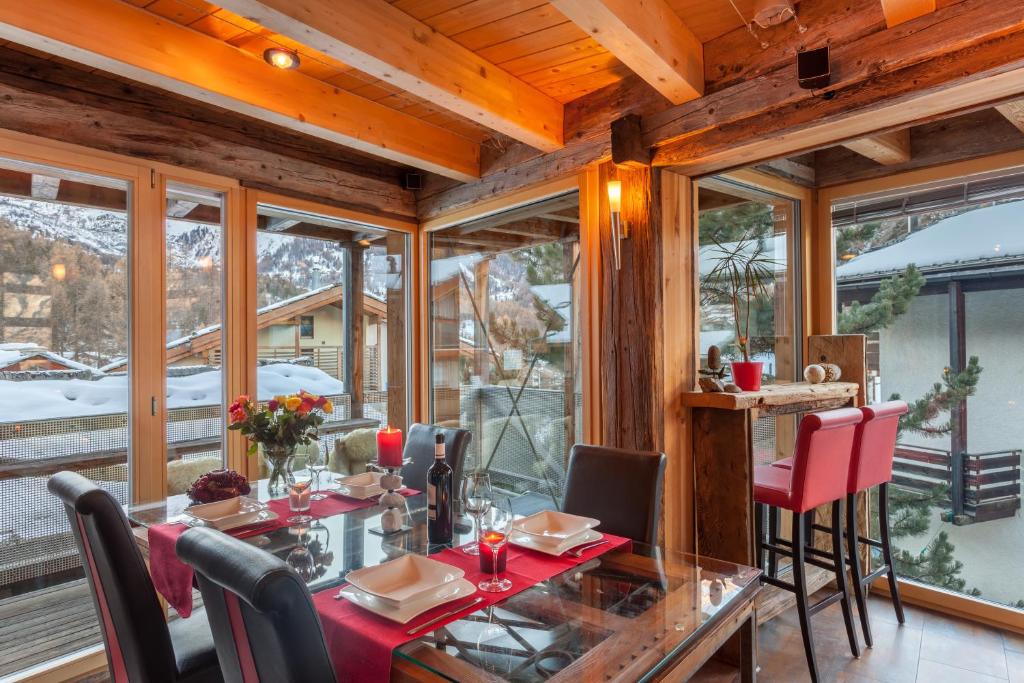 ein Esszimmer mit einem Tisch, Stühlen und Fenstern in der Unterkunft Chalet Schwalbennest in Zermatt