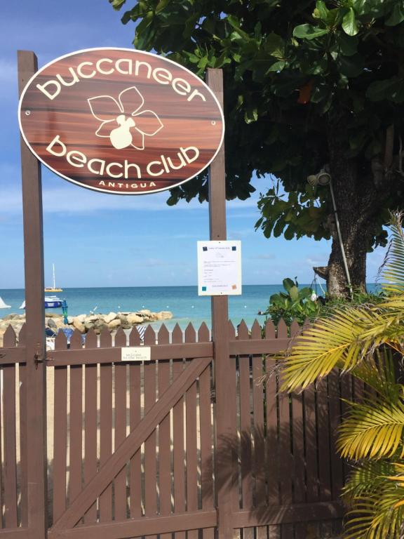 una señal para un club de playa con el océano en el fondo en Buccaneer Beach Club en Dickenson Bay