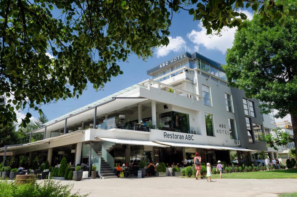 ein großes weißes Gebäude mit Leuten, die davor laufen in der Unterkunft Hotel ABC in Leskovac