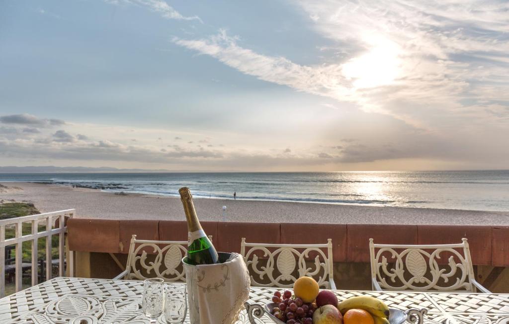 Jeffreys Bay的住宿－Jeffreys Bay Beach Accommodation，一张桌子,上面有一瓶葡萄酒和水果,在沙滩上