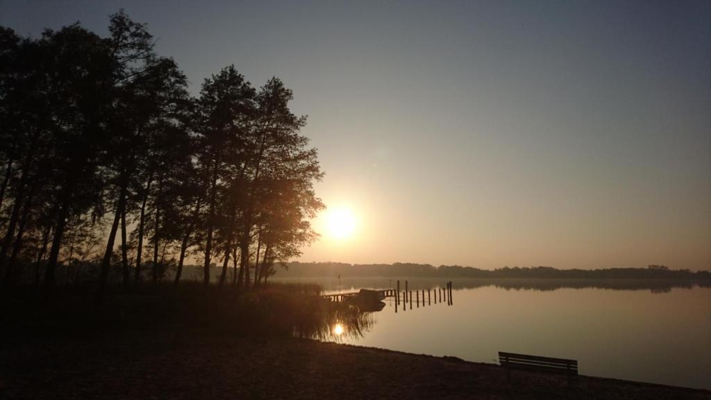 um pôr-do-sol sobre um lago com um banco e árvores em Fewoamglubigsee em Wendisch Rietz