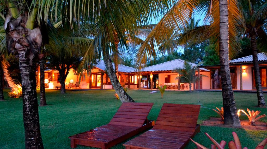 a wooden bench in front of a house with palm trees at Camauí Hotel in Barra Grande