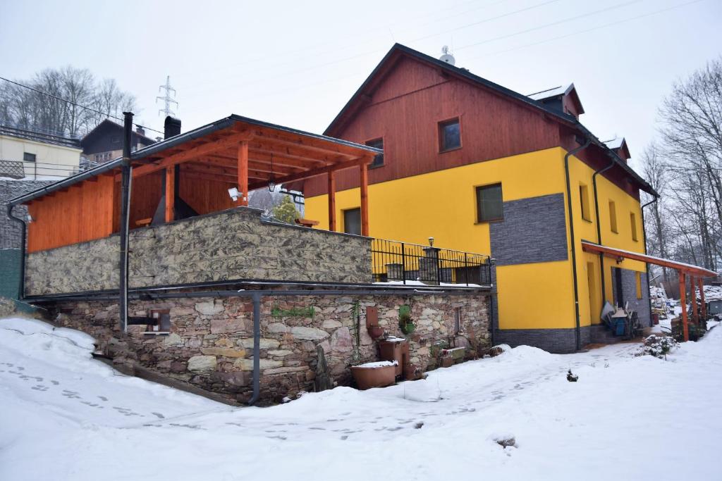 a yellow and red house in the snow at Apartmány Nad řekou in Svoboda nad Úpou