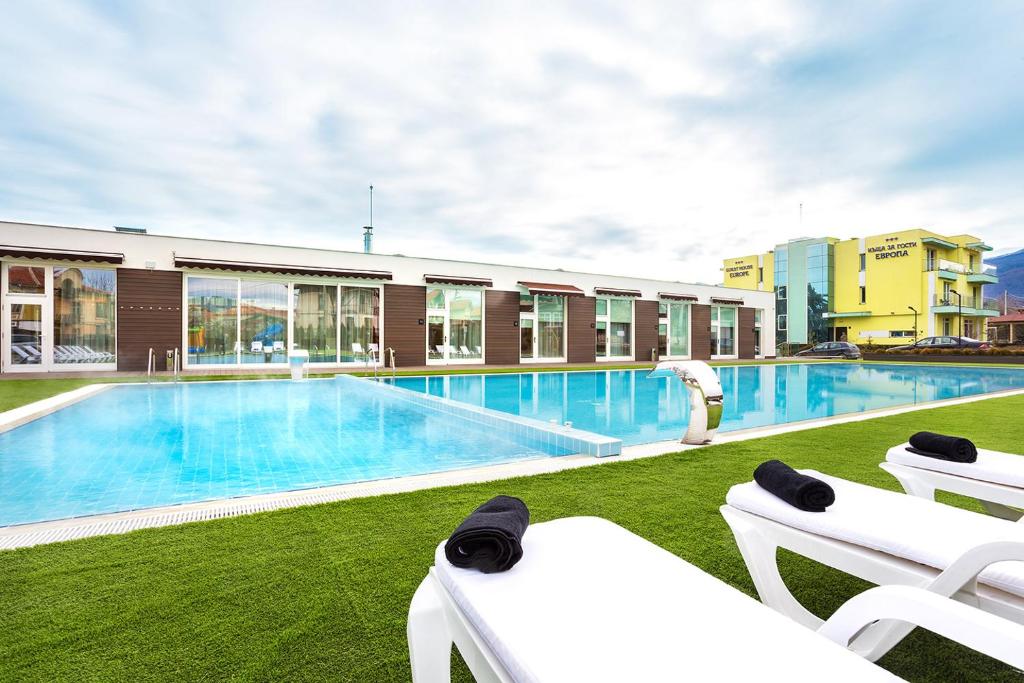 a swimming pool with white chairs and a building at Complex Europe in Dolna Banya