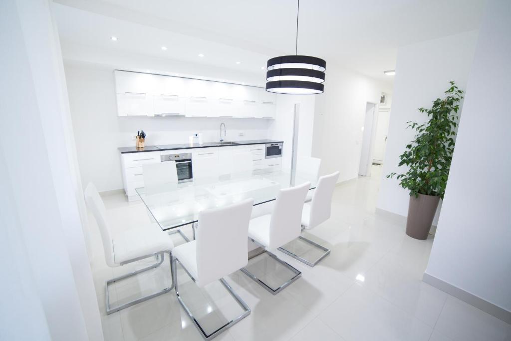 uma sala de jantar branca com uma mesa de vidro e cadeiras brancas em Bor Apartment em Bor