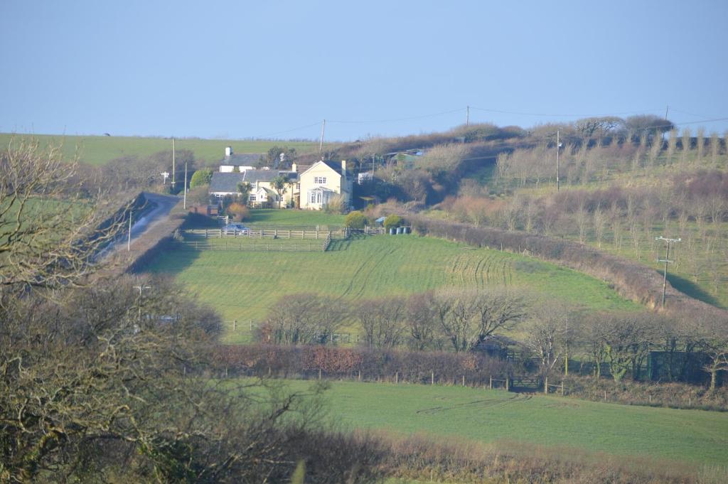 una casa en una colina con un campo verde en Bumble Bee Cottage en Hartland